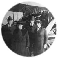 Circular black and white photo of 2 men and 2 women in front of an airplane
